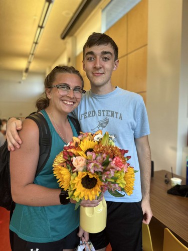 A young man and woman smile while holding flowers.
