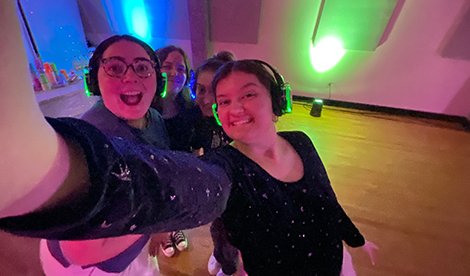 4 young women take a selfie while wearing wireless headphones.