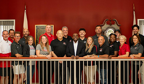 The Athletic staff and coaches smile with President Hayles