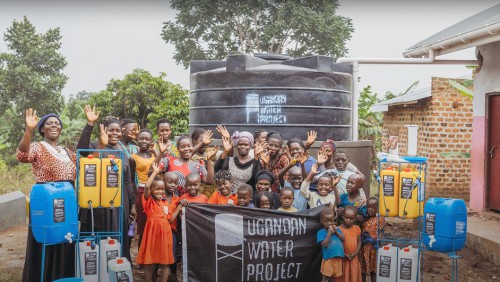 A group of Ugandan's smile and wave with a Ugandan Water Project banner.