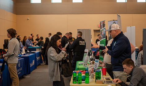 Employers stand behind tables while students speak with them.