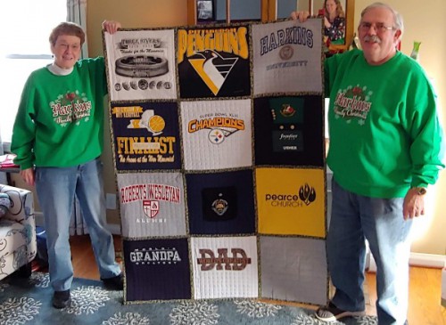 Glenn and Sue Harkins hold up quilt made of sports team tshirts.