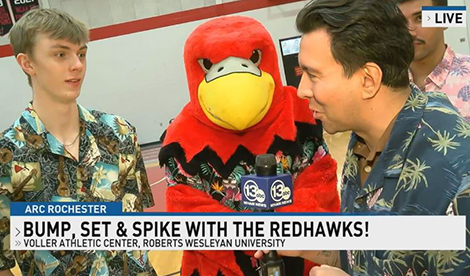A men's volleyball player is interviewed by Chris Lopez. Reggie the Redhawk stands in between the 2. Bump, set & spike with the Redhawks!
