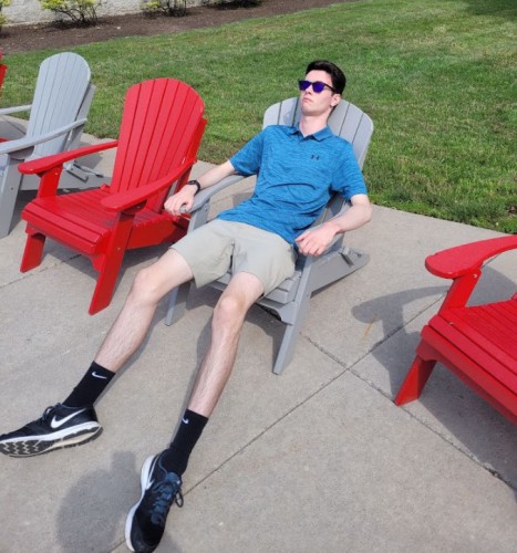 Nate lounges in a gray adirondack chair on campus.