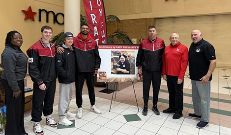 Roberts athletes and athletics staff smile in front of a Pirate Toy Fund sign.