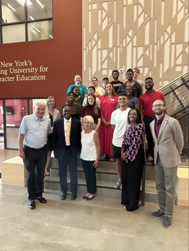 Students, staff, Tom Golisano, and President Hayles stand on steps in the Golisano Community Engagement Center and smile for a photo.