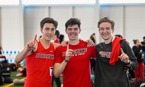 3 young men wear Roberts track gear and hold up their index fingers.