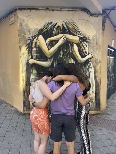 Three students hug before a mural.