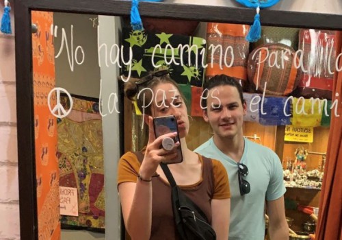 A young woman takes a selfie in a mirror while making a kissing face while a young man smiles next to her.